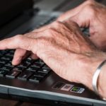 Staré ruce píší na klávesnici notebooku