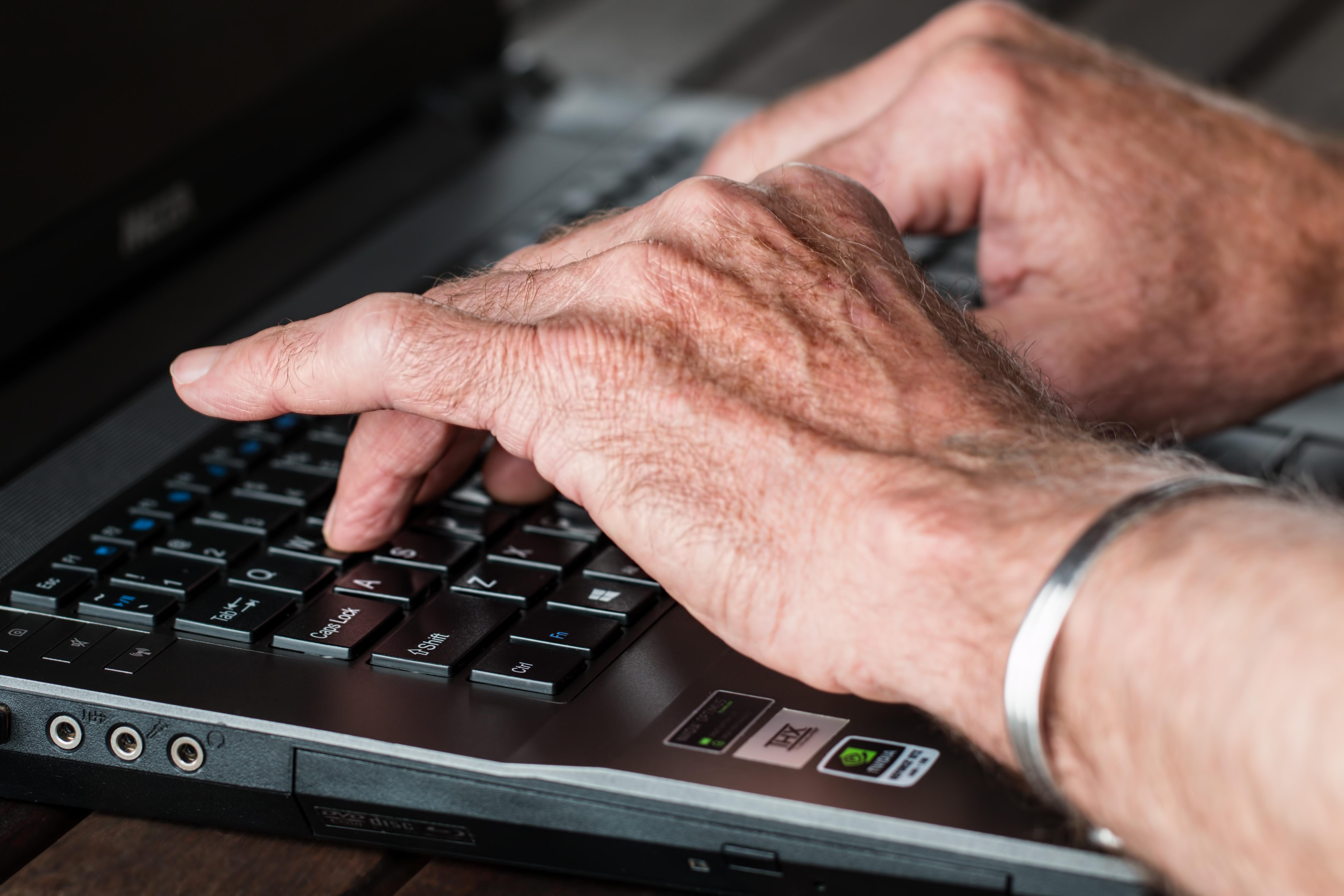 Staré ruce píší na klávesnici notebooku